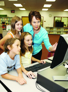 A teacher instructing kids on using the computer.